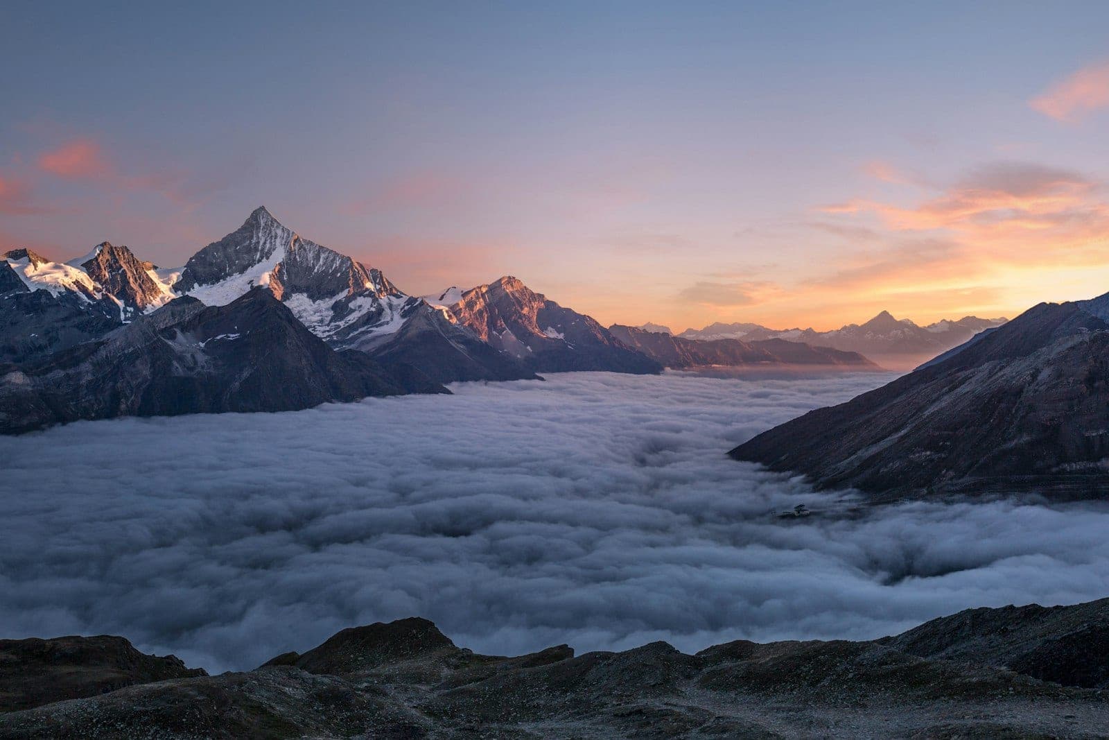 Snow-dusted mountain peaks rising from a sea of clouds at sunset
